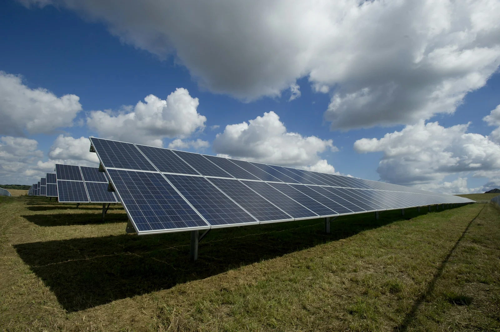 Solar panels in an open field beneath a cloudy sky.