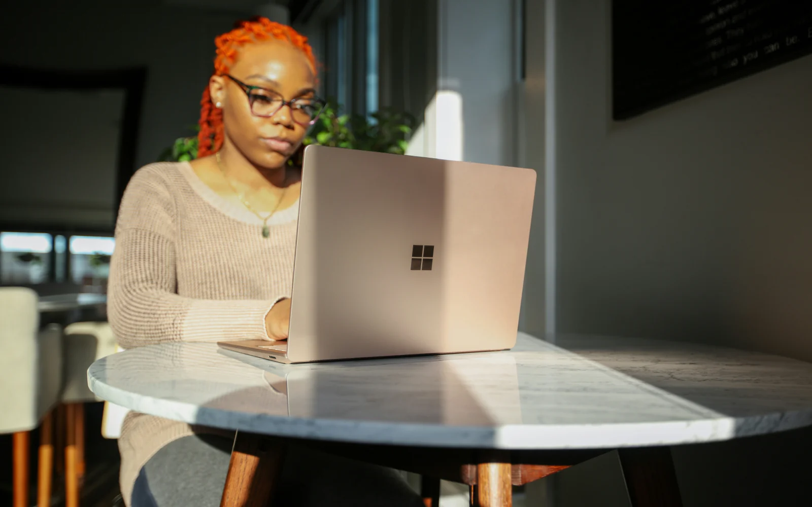 A woman working on a laptop in warm window light.