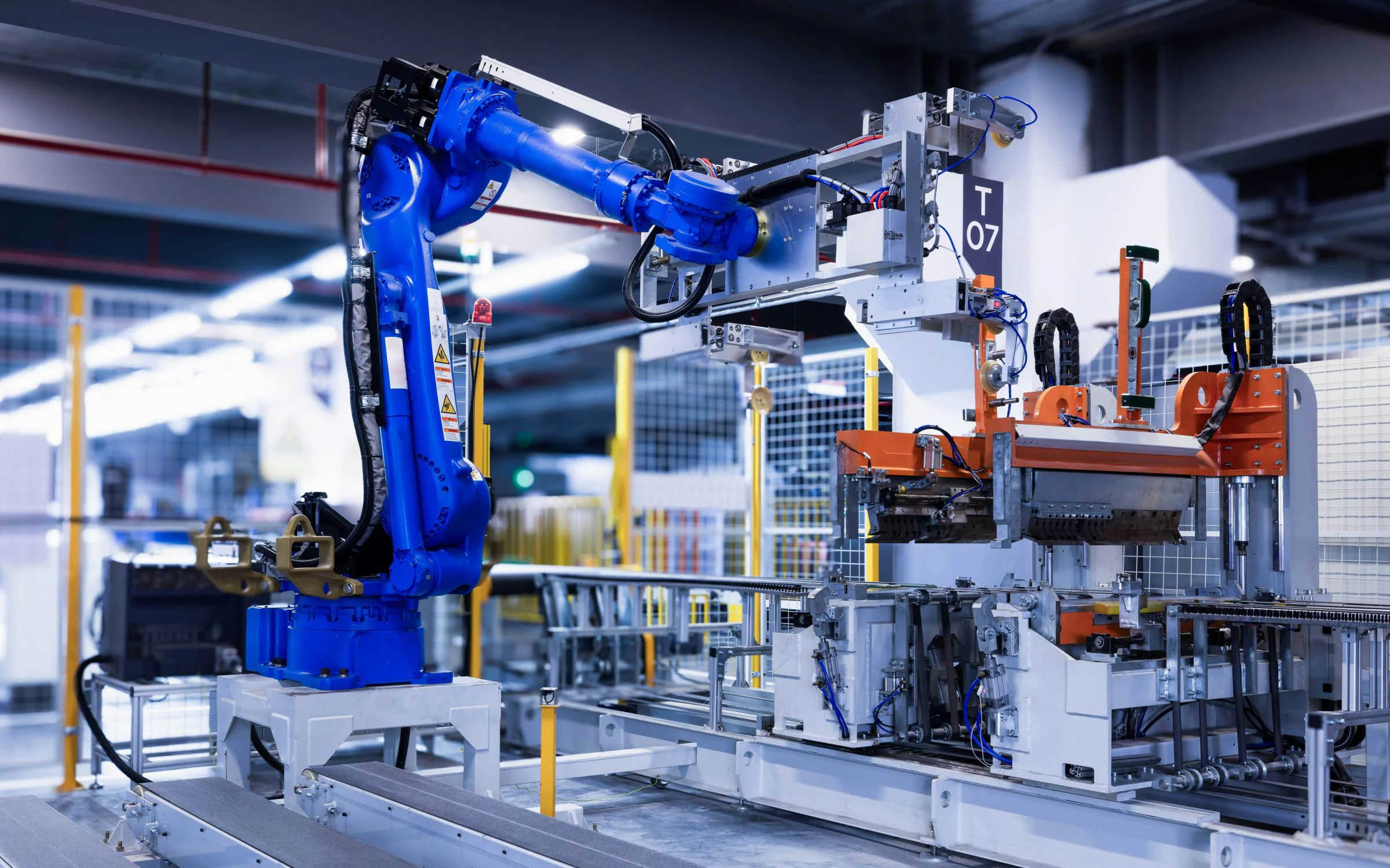 A blue robot arm and an orange press on an automated production line